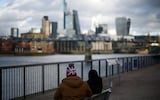 People sit alongside the bank of the River Thames with the City of London financial district in the background, in London, Britain, January 13, 2023.